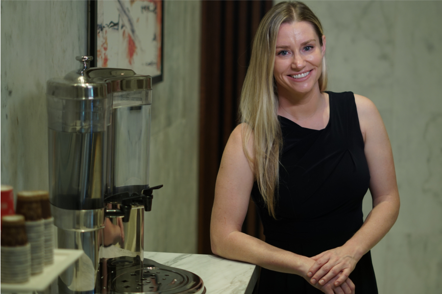 Smiling woman standing beside coffee table ready for Project Ultimate Life speaking engagement